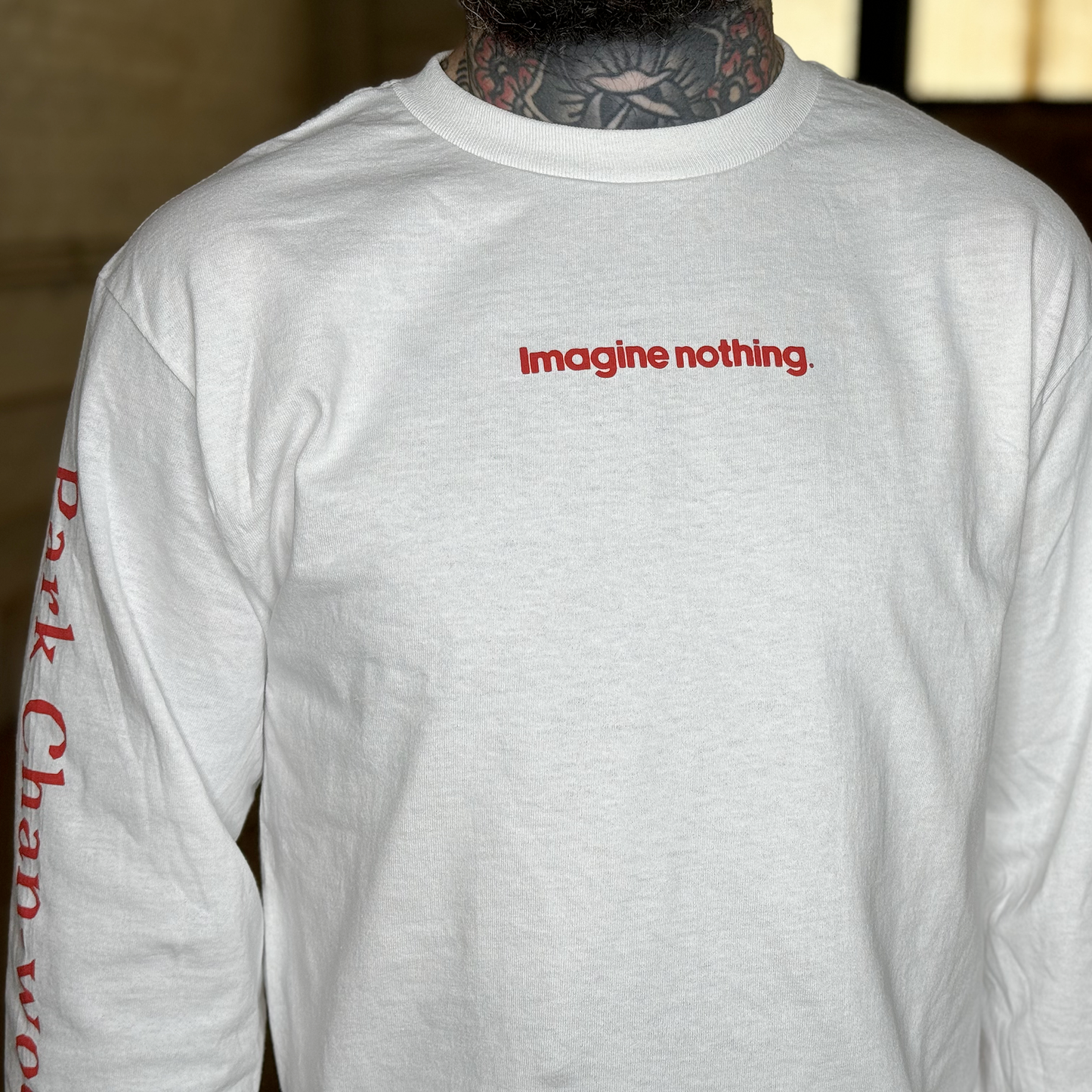 Zoomed in model photo of the front of the shirt, with the left sleeve slightly visible. The front of the shirt reads "Imagine nothing." in a very small, centered, red text.