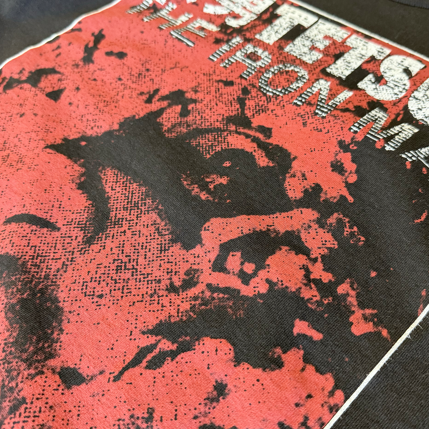 Zoomed in detail of the black version of the shirt. It has a distorted image of the main character printed in red, and reads "Tetsuo The Iron Man" in white with a white border.