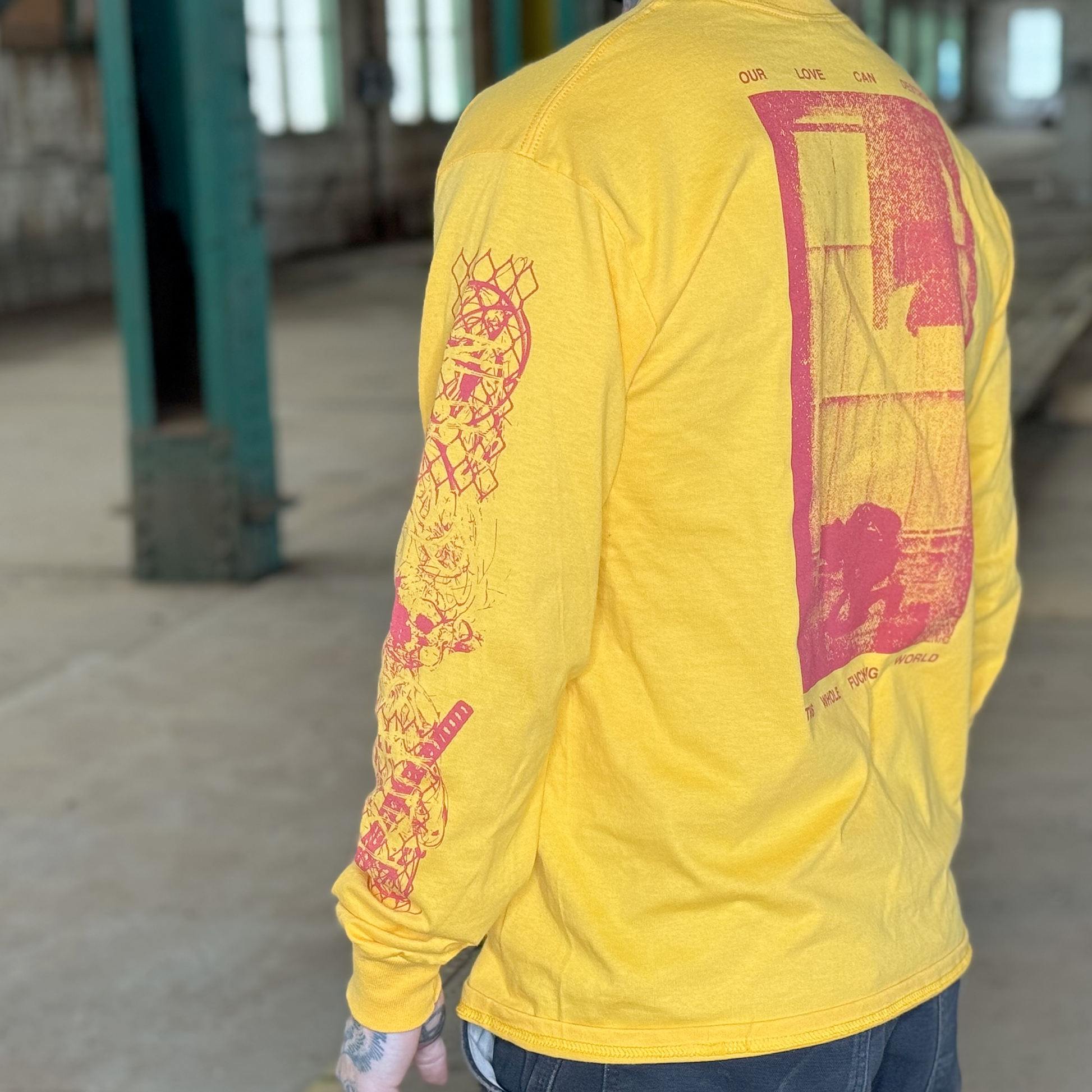A zoomed in model photo of the back and one sleeve of the yellow shirt. The print is red, and features metal and chain links collaged on the sleeve.
