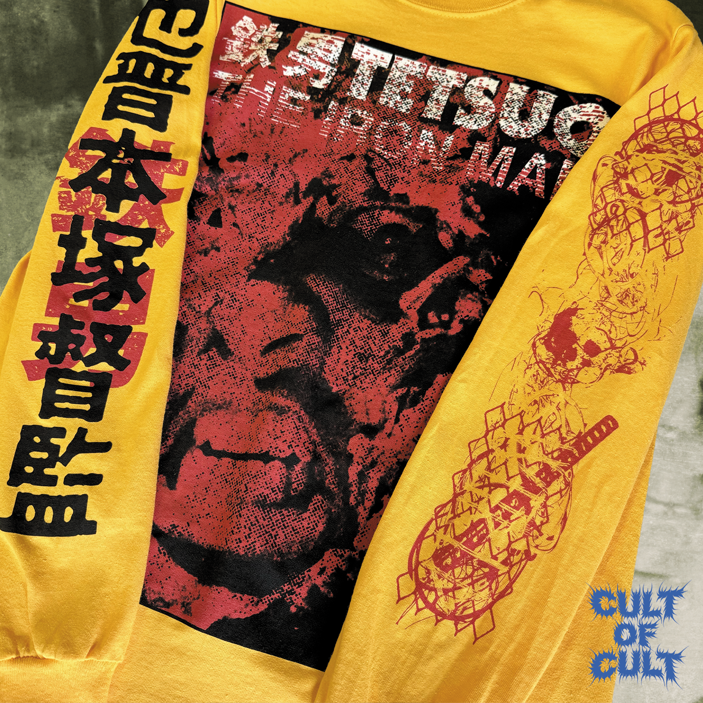 The front and sleeves of the yellow version of the shirt. There is a zoomed in detail shot of both sleeves. One sleeve has the movie title and directors name in Japanese characters. The other sleeve features a collage of metal and chain link.